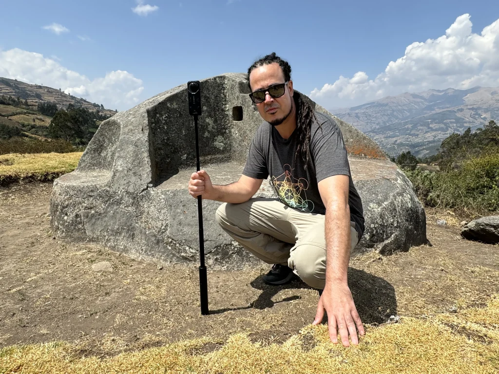 Anyextee kneeling in front of ancient Andean stone seat with camera gear in Peru